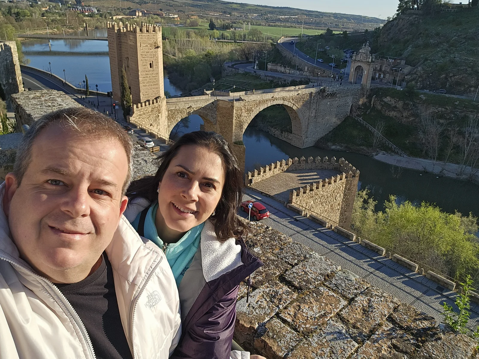 Casal em primeiro plano; contexto urbano ao fundo.